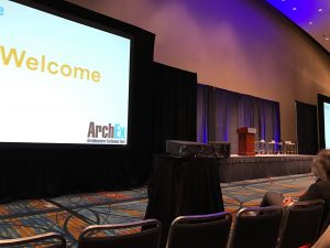 The Empty stage and a screen showing a slide welcoming the attendees to ArchEx2016